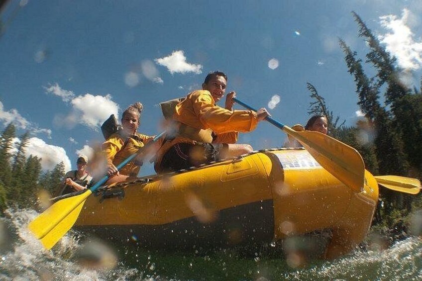 A group of people in a yellow raft with paddles, navigating through water. 2