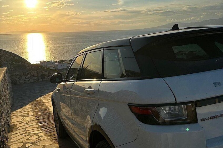 A white SUV parked on a stone path by the sea during sunset. 4