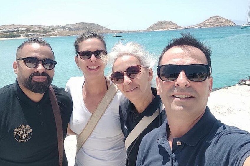 A group of people taking a selfie by a beach with clear blue water and distant hills. 2