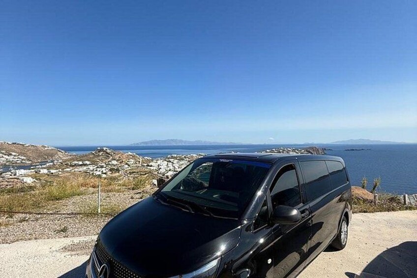 A black van parked on a coastal road with a scenic view of the sea and distant mountains. 5