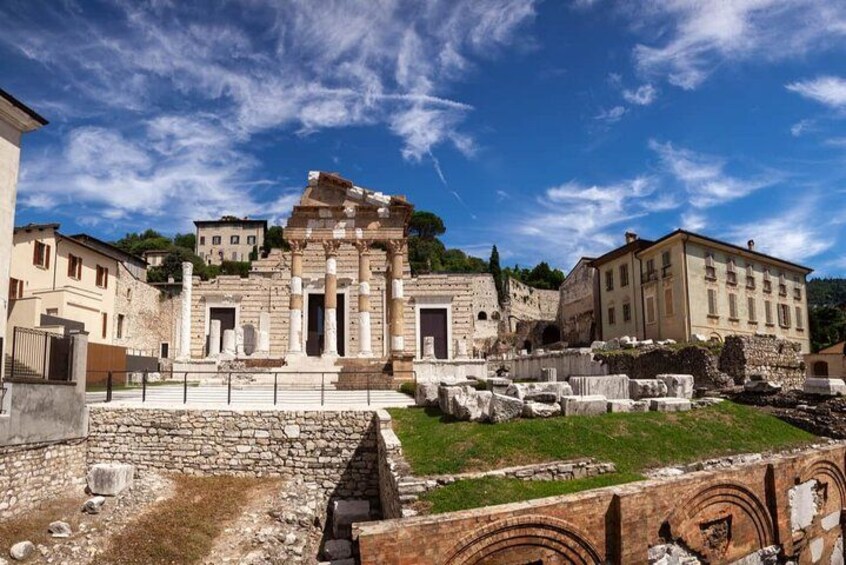 Ancient ruins with columns and stone structures, surrounded by modern buildings and a clear sky. 1