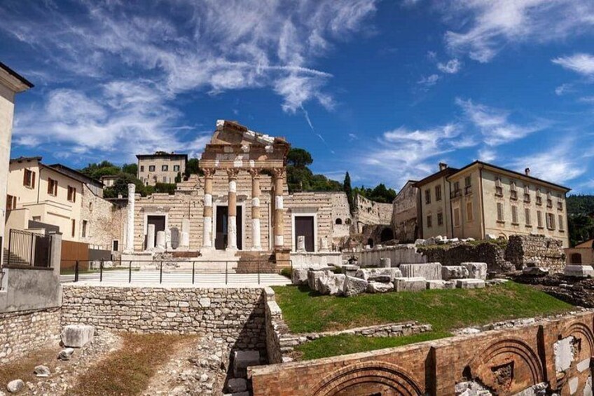 Ancient ruins with columns, a stone wall, and modern buildings in the background. 1