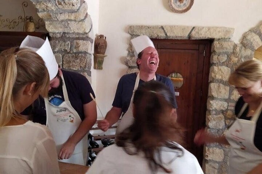 Un grupo de personas en una cocina, algunas con gorros y delantales de chef, con paredes de piedra y una puerta de madera al fondo. 3