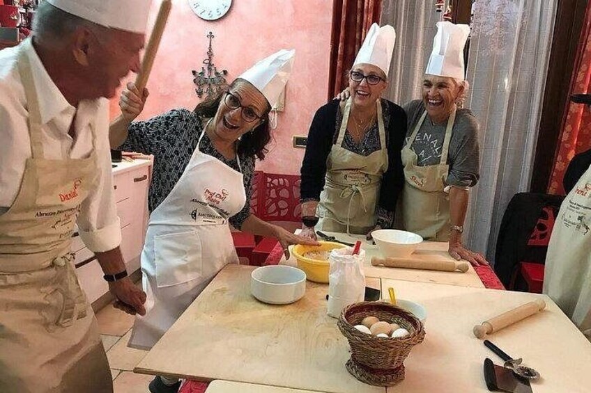 A group of people in aprons and chef hats, engaged in cooking activities with bowls, eggs, and a rolling pin on a table. 2