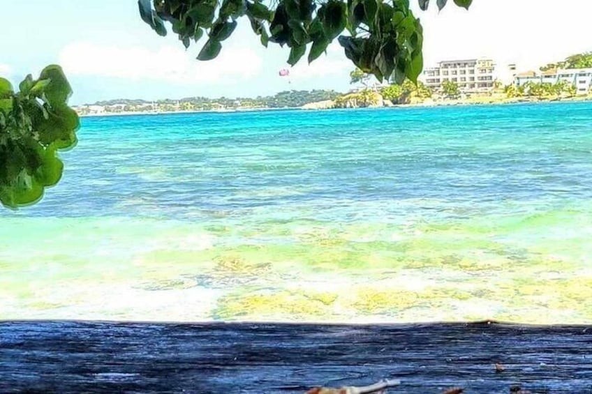 A coastal scene with clear turquoise water, a sandy beach, and a building in the background. 2