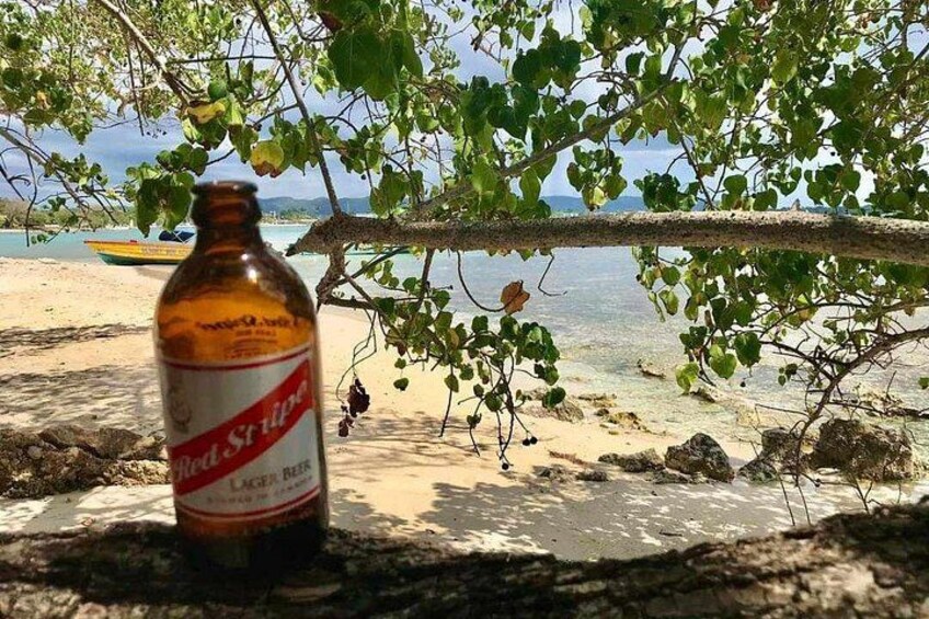 En Red Stripe øl på en strand med et træ og en båd i baggrunden. 3