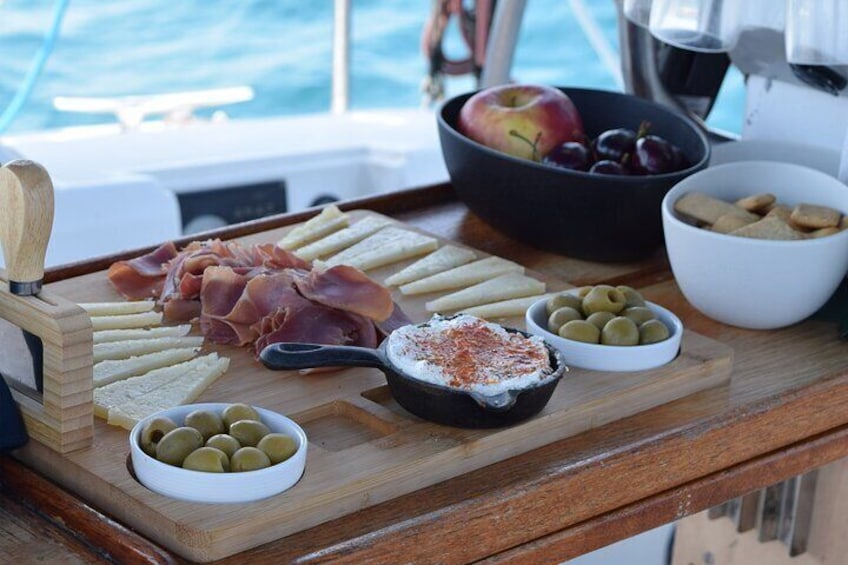 A wooden tray with various foods including prosciutto, olives, and a bowl of olives. 5