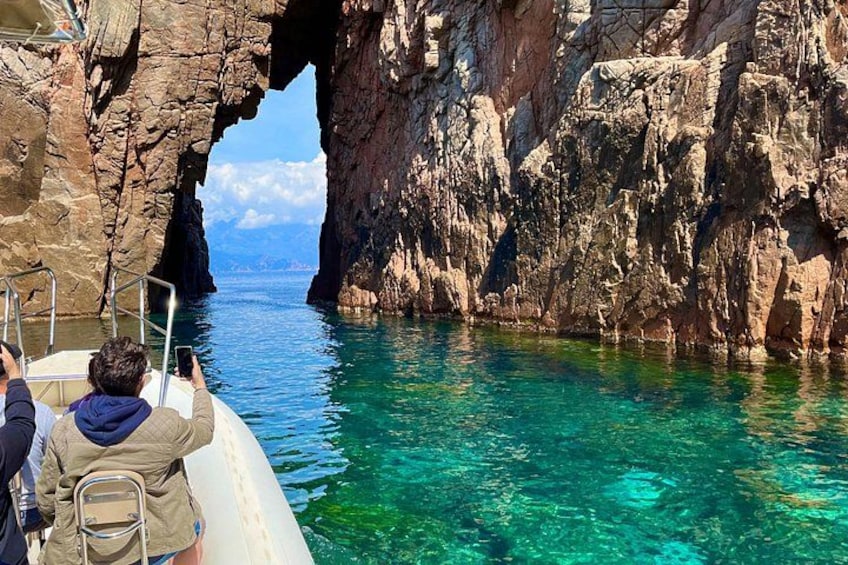 A boat near a rocky coastline with a clear blue sea and a large rock formation. 5