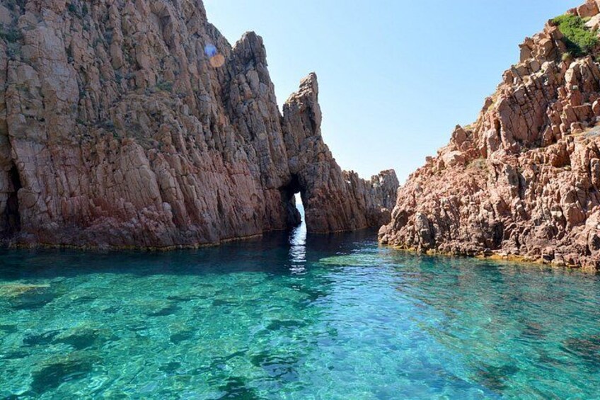 A coastal landscape with clear turquoise water, rocky cliffs, and a narrow passageway. 1
