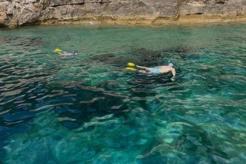 Two people snorkeling in clear blue water with rocky cliffs in the background. 2