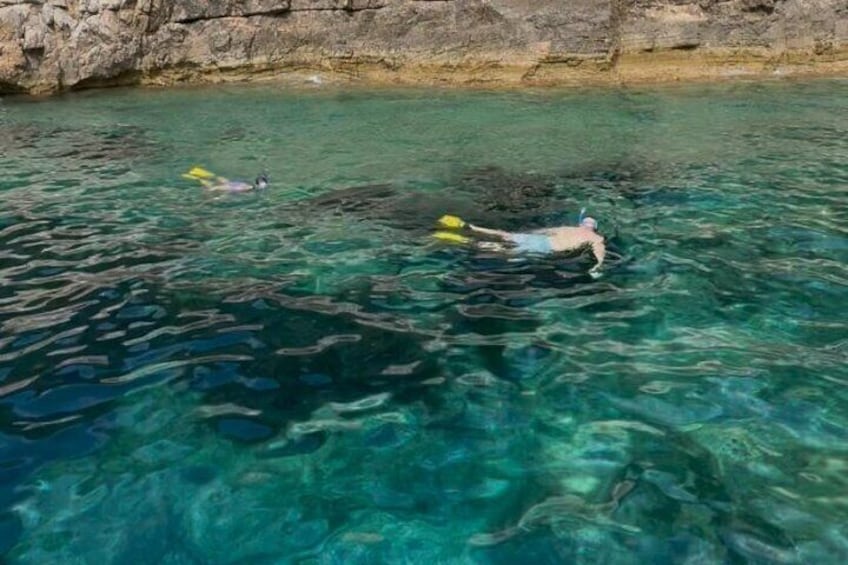Two people snorkeling in clear water with rocky cliffs in the background. 4