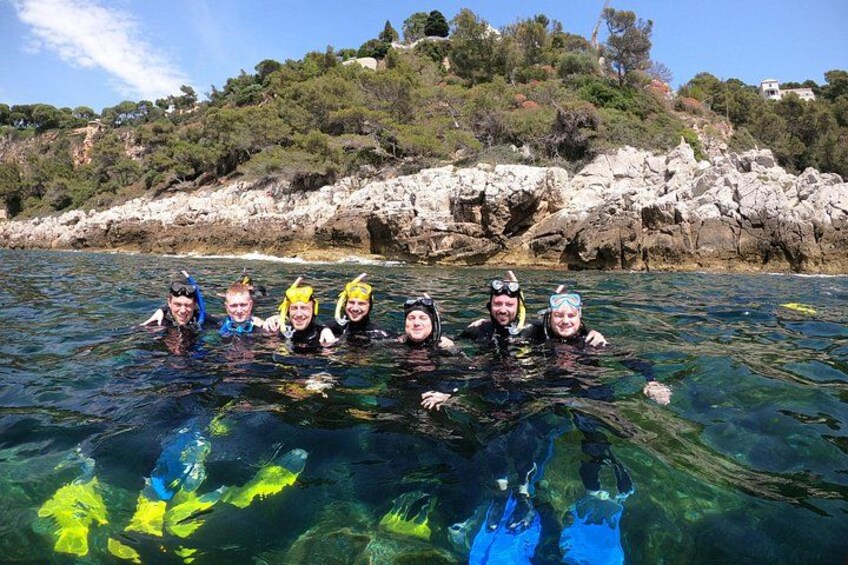 A group of people snorkeling in clear water with a rocky coastline and greenery in the background. 3