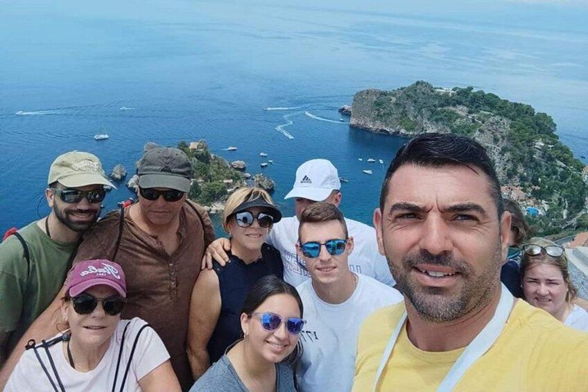 Un grupo de personas en un acantilado contemplando una zona costera con barcos y una pequeña isla. 1
