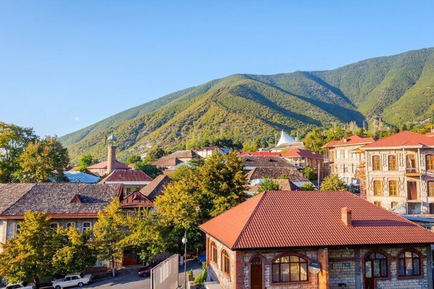 A town with red-roofed buildings, a church, and mountains in the background. 3