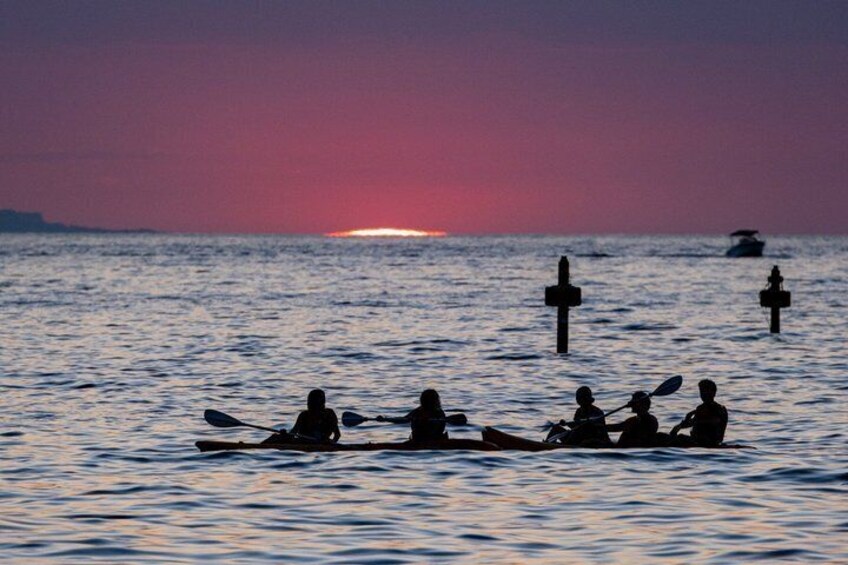 A sunset over calm waters with people paddling in a rowboat. 4