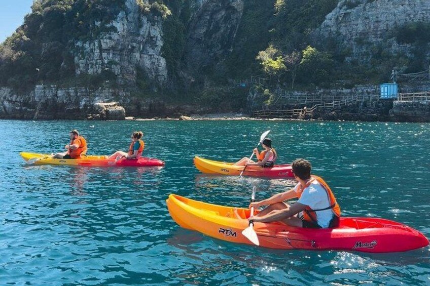 People kayaking on a calm sea with rocky cliffs in the background. 3