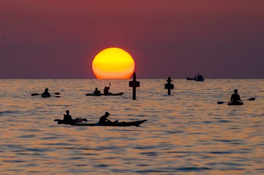 A sunset over a calm sea with several kayaks and a boat. 2