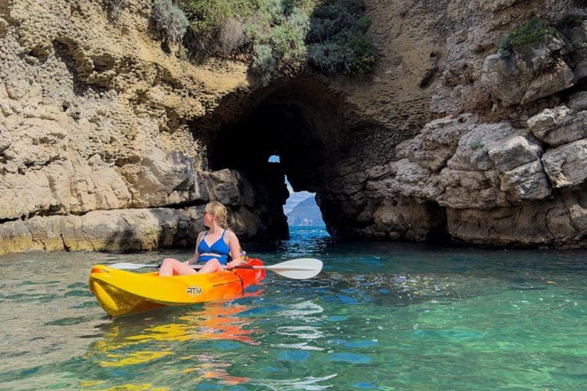 A person in a yellow kayak near a rocky cave entrance. 1