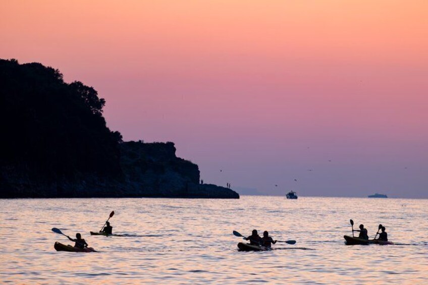 A sunset over a calm sea with kayakers and a distant boat. 5