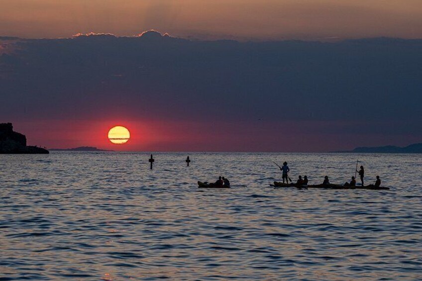 A sunset over a calm sea with people on small boats. 3