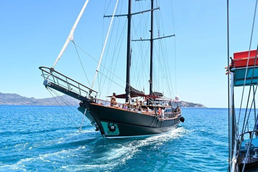 A sailing boat on a clear blue sea with a mountainous coastline in the background. 2