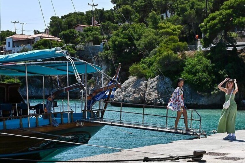 A boat docked at a pier with a rocky coastline and houses in the background. 3