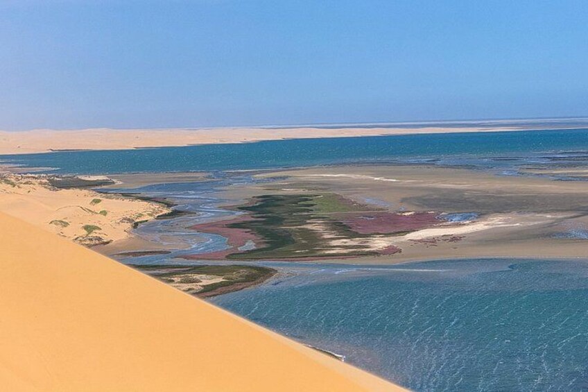 A coastal landscape with sand dunes, a beach, and a water body. 1