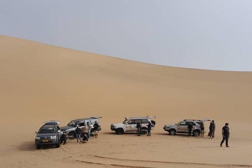 A desert landscape with sand dunes and several off-road vehicles parked on the sand. 5