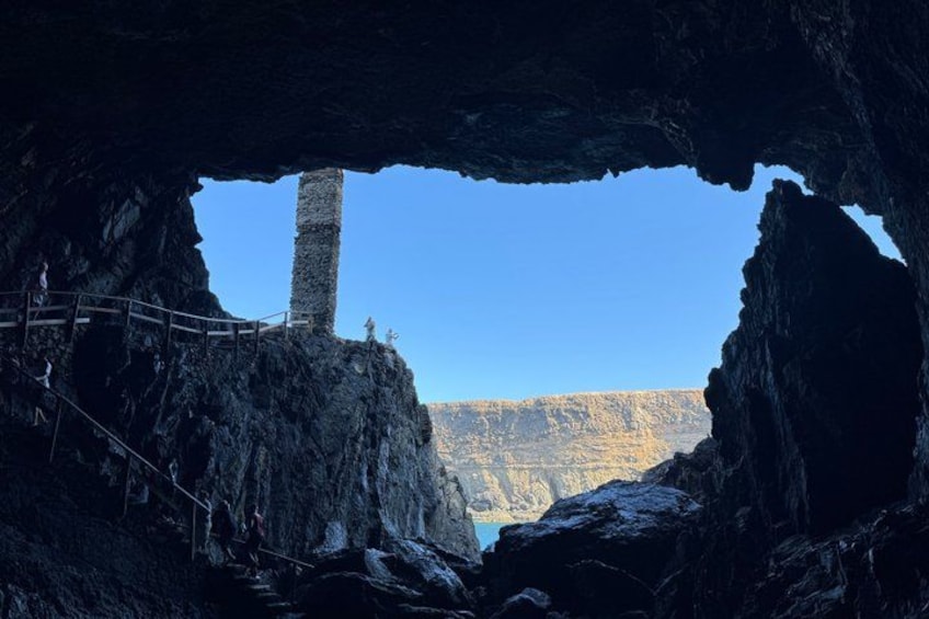 A cave entrance with a stone pillar, a wooden walkway, and a view of a mountain range. 5