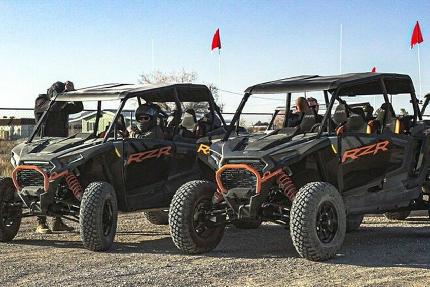 Two off-road vehicles with 'RZR' branding parked on a gravel surface. 5
