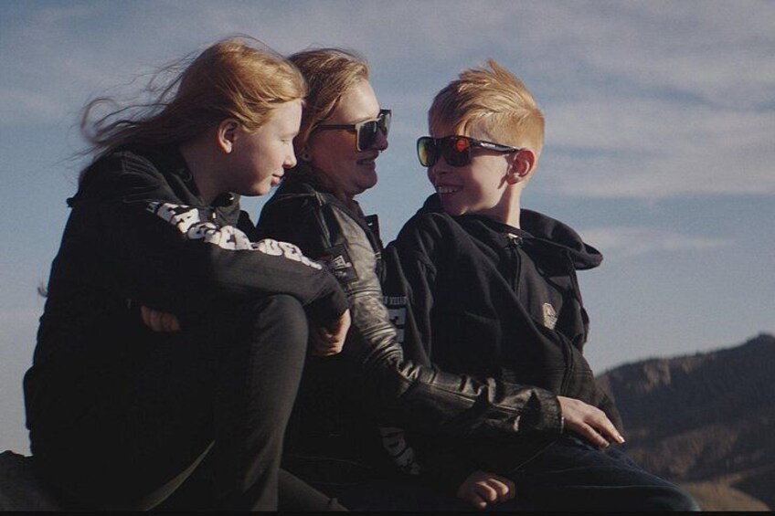 Three people sitting on a rock with a mountainous landscape in the background. 3