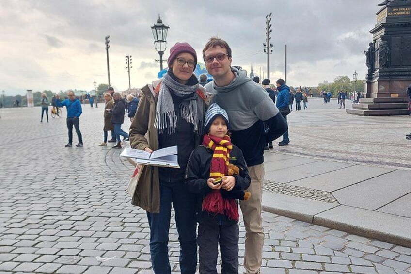 A family with a child in a public square with cobblestone pavement, a statue, and a lamppost. 4
