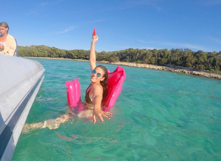 Una persona in barca con galleggianti rosa, circondata da acque cristalline turchesi e da una costa rocciosa con alberi. 4