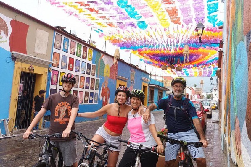 Een groep mensen op fietsen in een kleurrijke straat met muurschilderingen en een levendige hemel. 2
