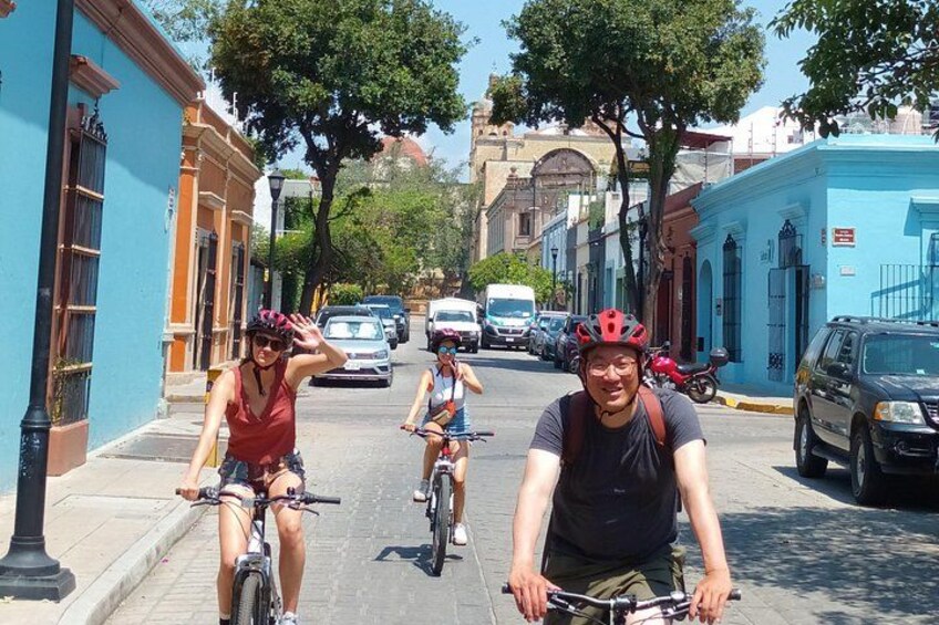 Three cyclists on a city street with buildings and parked cars. 2