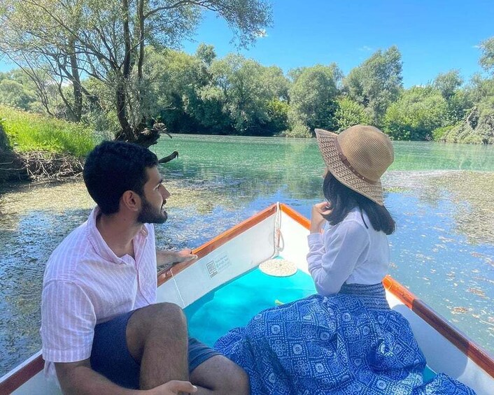 Two people on a boat in a river surrounded by greenery. 1