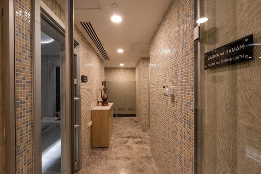 Un couloir aux murs carrelés, un comptoir en bois et un panneau indiquant la présence d’un sauna et d’un bain turc. 4