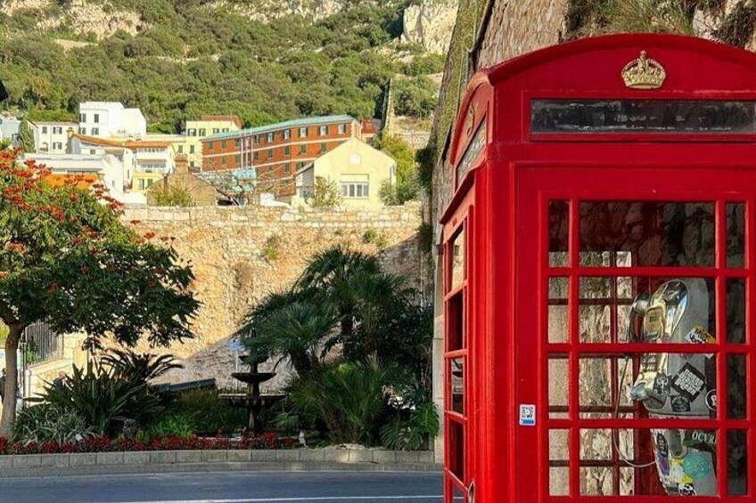 A red telephone booth with a stone wall and greenery in the background. 4