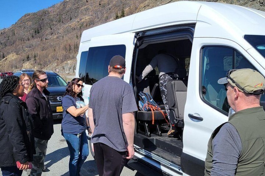 A white van with its back door open, luggage inside, and people standing around. 5