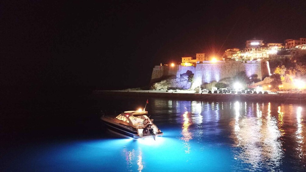 A boat on calm water near a brightly lit coastal town at night. 2