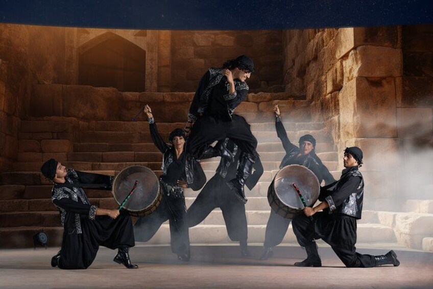 A group of people in black attire performing a traditional dance with drums in an ancient stone building. 4