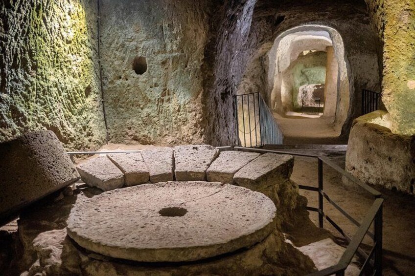 Una estructura circular de piedra con escalones que conducen hacia ella, rodeada de muros de piedra tosca y una barandilla metálica. 3