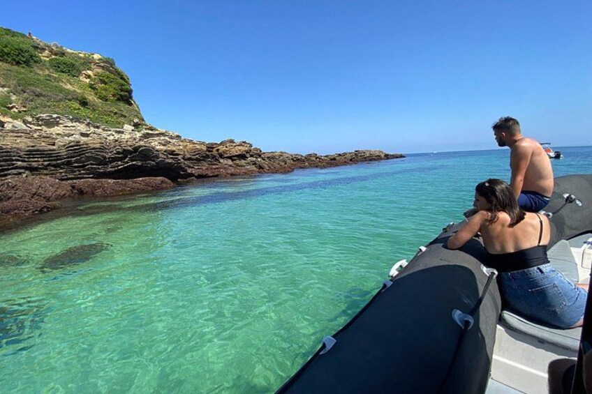Un bateau sur une eau turquoise et limpide, une côte rocheuse et un ciel dégagé. 1