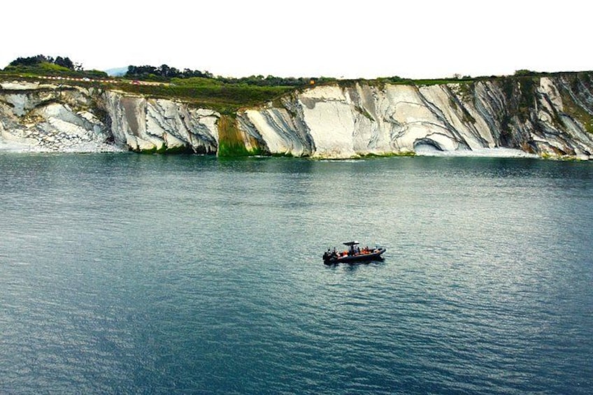 A boat on calm water near cliffs with white and green layers. 3