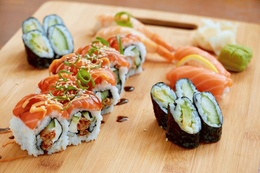 A wooden cutting board with various sushi pieces, including rolls with salmon and cucumber. 1