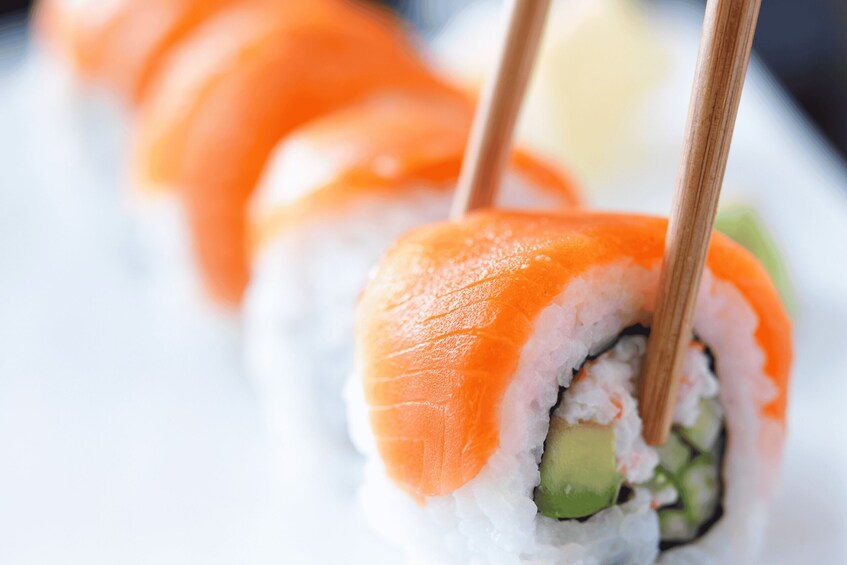 A sushi roll with salmon and avocado, held by chopsticks. 3