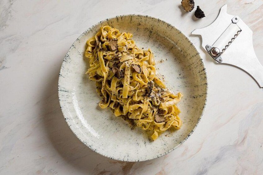 A plate of pasta with mushrooms, a pasta cutter, and some mushrooms on a marble surface. 3