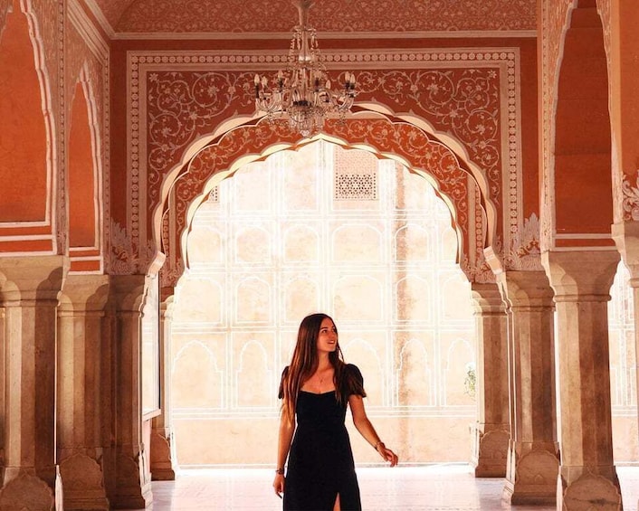 Una persona de pie en un salón majestuoso y ricamente decorado, con arcos y columnas. 2