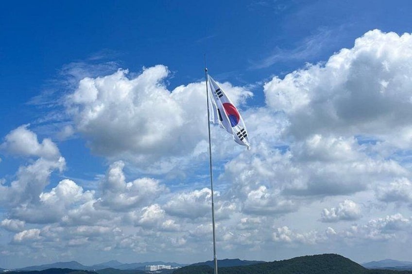 Un asta con una bandera, un cielo azul despejado y una cadena montañosa al fondo. 2