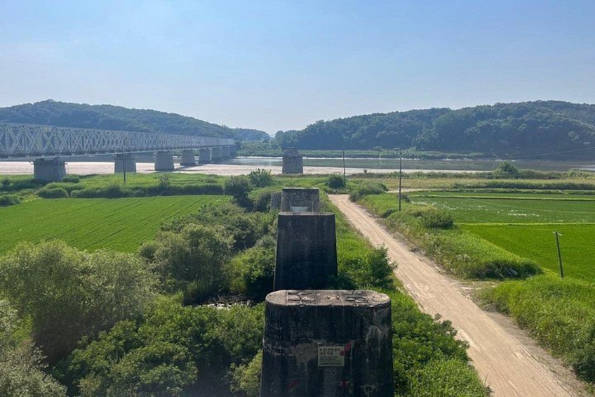 Un puente, un camino de tierra y campos verdes. 4